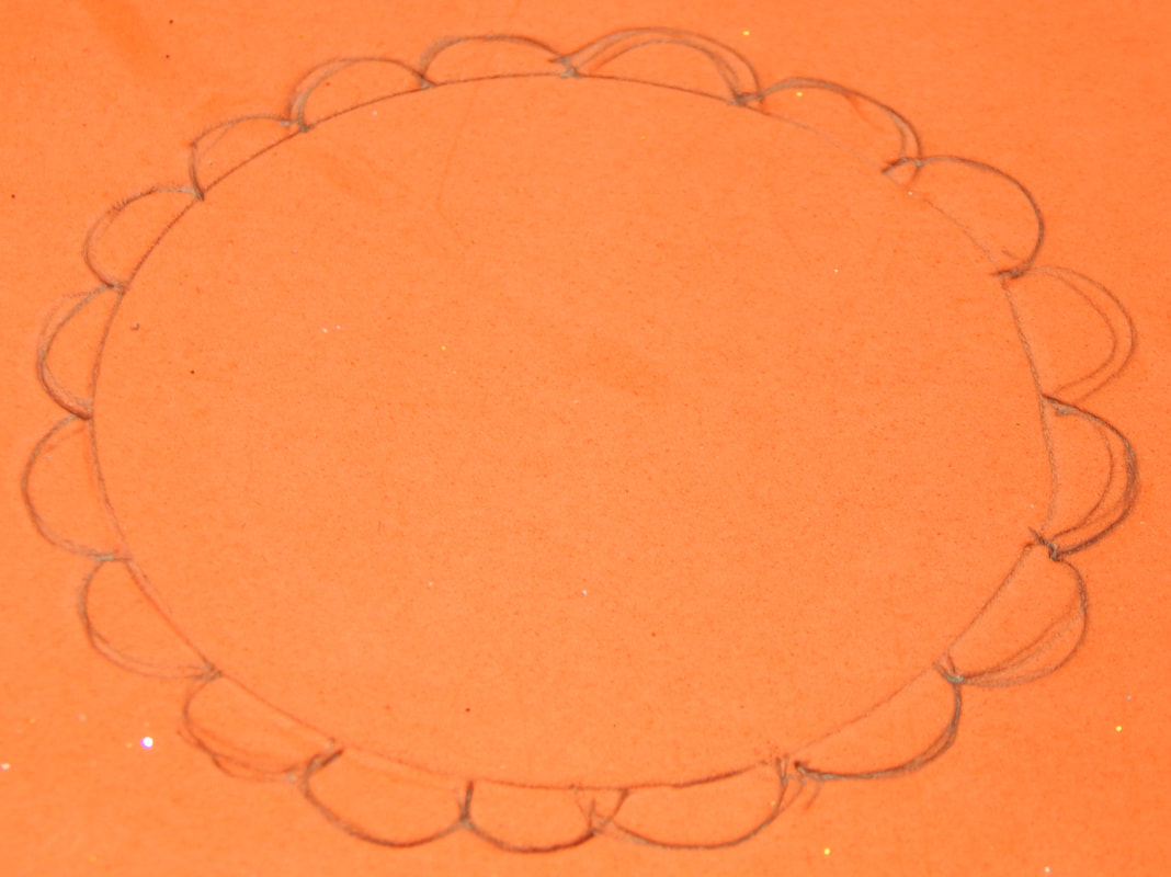 An outline of a circle with scalloped edges drawn around it in pencil on a piece of red craft foam