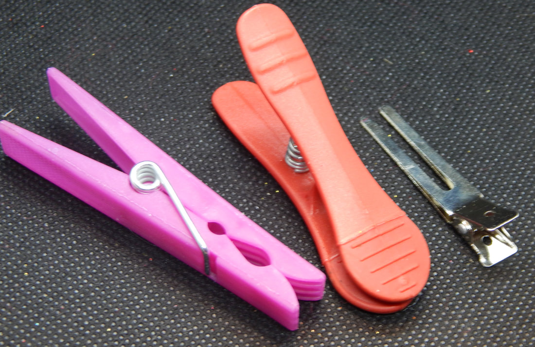 A pink clothespin, red clothespin, and silver hair clip on a black background