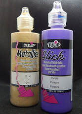 A bottle of gold paint and a bottle of purple paint on a black background