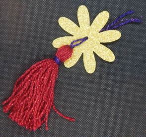 A gold glitter craft foam flower with a tassel placed at the center