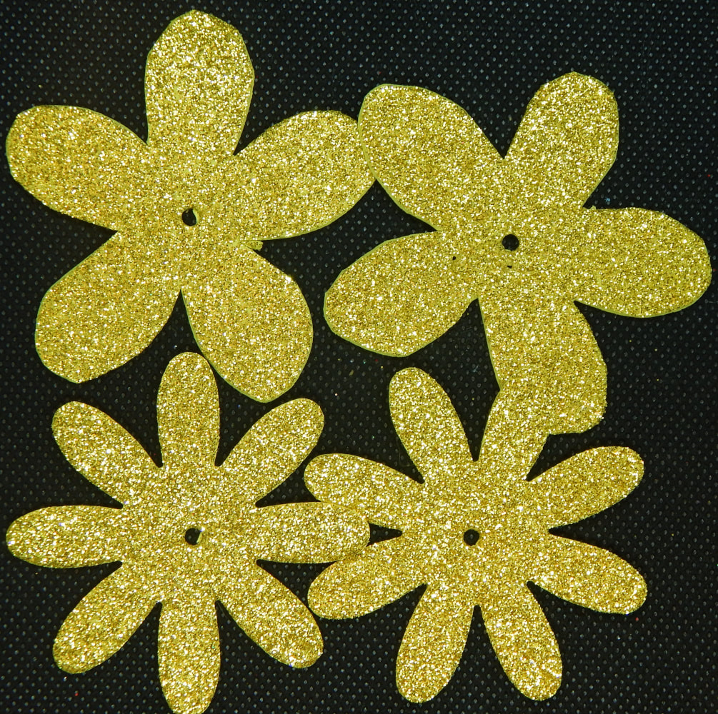Four glitter gold flowers on a black background the top two have five rounded petals, the bottom two have eight skinnier petals. All four have a small hole in the center