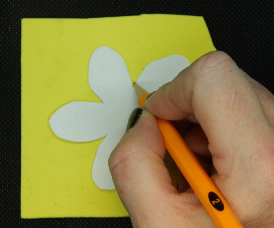 A hand tracing around a flower patter on yellow foam with a yellow pencil