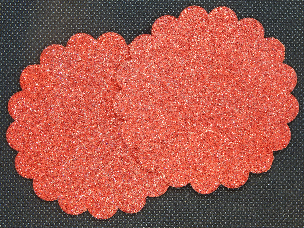 Two circles of red glitter craft foam with scalloped edges on a black background 