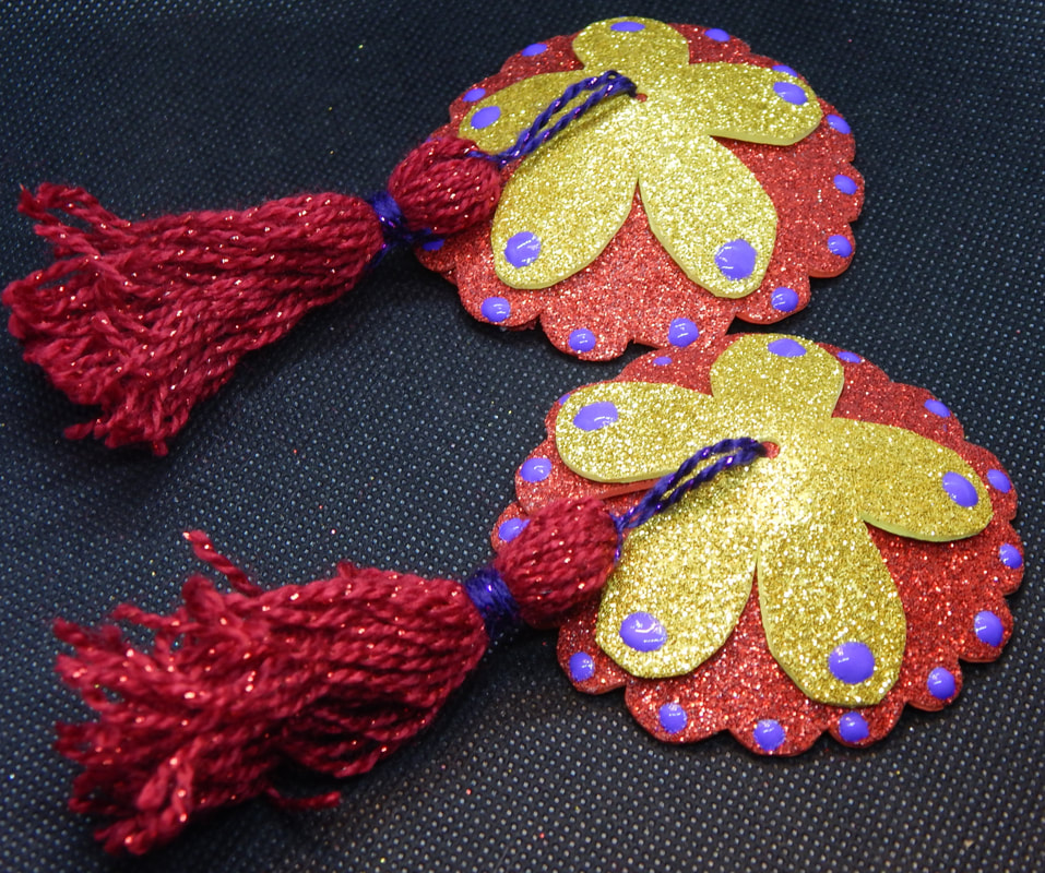 A pair of red and gold pasties with purple dots on them and red tassels on a black background 