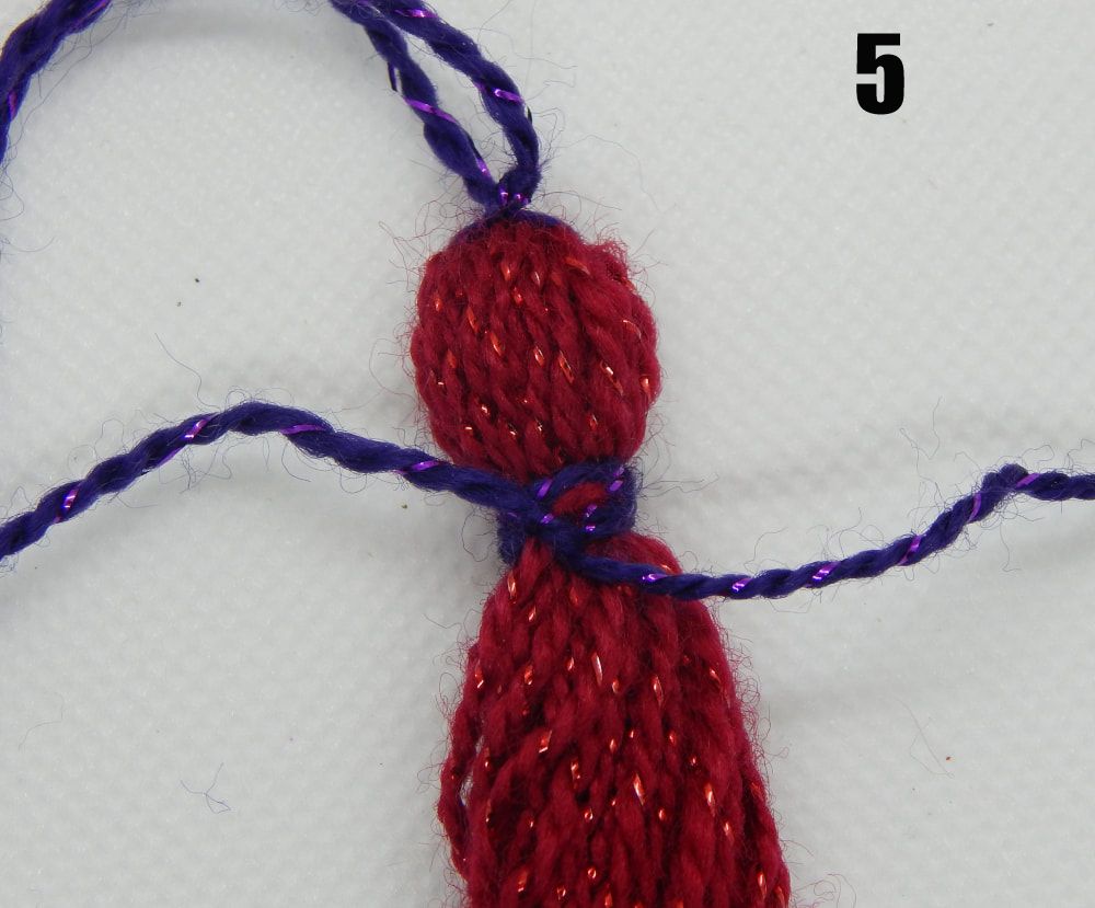 A group of red threads is gathered with purple threads both at the top and about an inch down, creating the top of a tassel