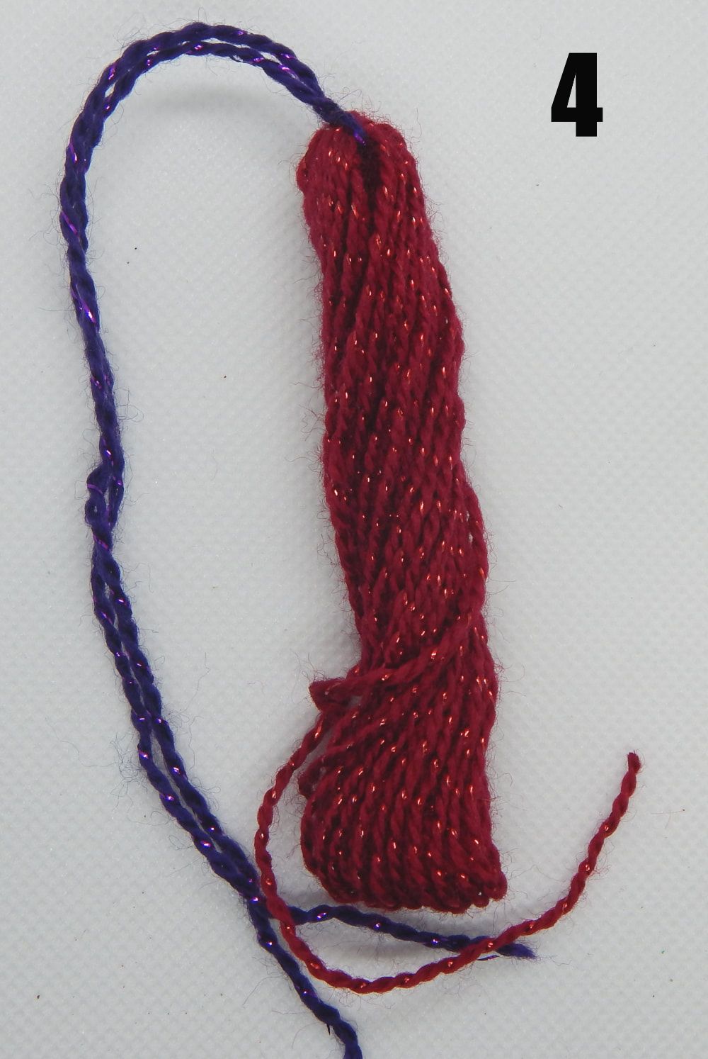Multiple loops of red yarn are held together with a knotted piece of purple yarn. There is a 4 in the upper right hand corner of the picture.