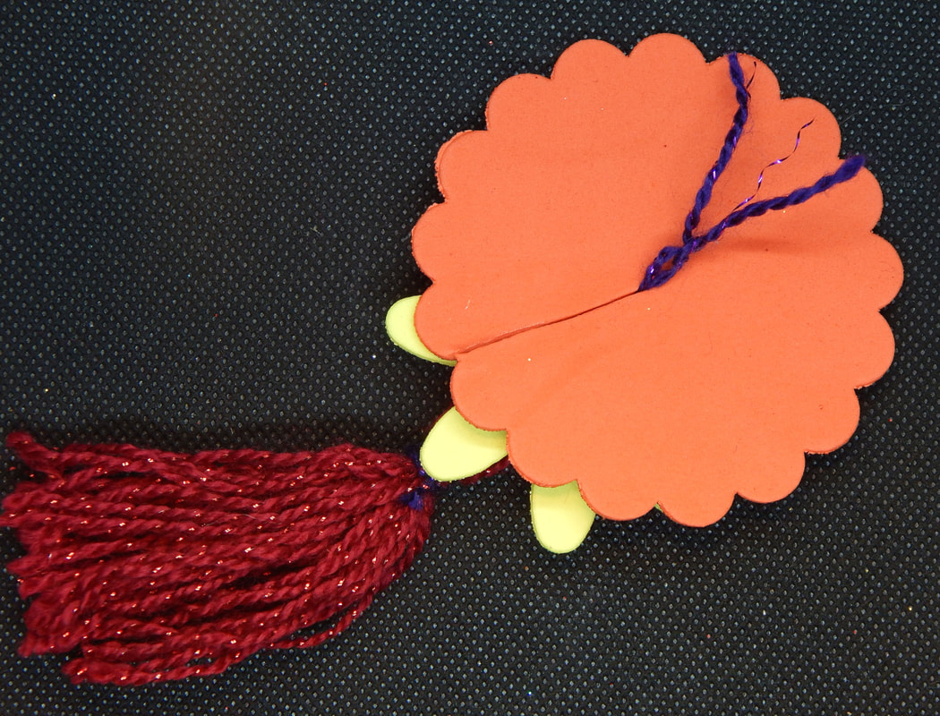 A picture of the in progress pastie from the back with top string of the tassel pulled through the slit. A part of the gold flower can also be seen peeking out